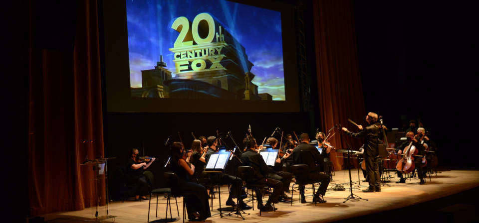 Cenas icônicas de filmes e séries são projetadas no teatro enquanto Orquestra Sesiminas toca trilhas sonoras famosas ao vivo