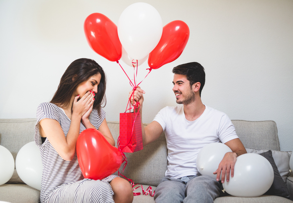 Main man handing his girlfriend balloons red bag