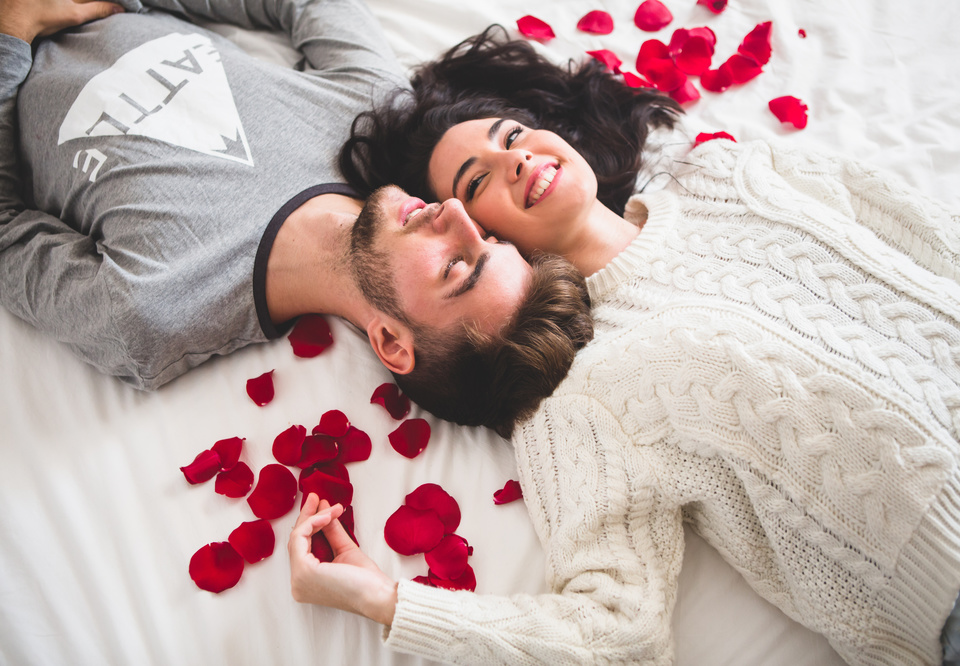 Main couple lying bed head with head surrounded by rose petals