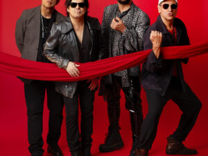 Quatro integrantes da banda Barão Vermelho posam em frente a um fundo vermelho. Todos usam roupas escuras e óculos escuros. Um tecido vermelho atravessa a imagem na horizontal, sendo segurado por dois dos músicos. A expressão dos integrantes é séria e confiante, refletindo atitude e estilo.