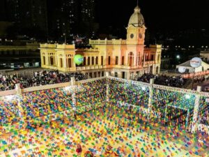 Vista aérea da Praça da Estação, em Belo Horizonte, decorada com bandeirinhas coloridas e arquibancadas lotadas durante o Arraial de Belô à noite.