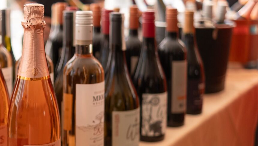 Garrafa de espumantes e vinhos brasileiros dispostas em fileiras sobre uma mesa coberta com toalha bege durante o festival Vinho na Vila.