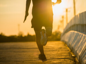 Pessoa correndo em uma via urbana ao entardecer, com o sol se pondo ao fundo e iluminação dourada sobre o asfalto.
