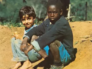 Dois meninos sentados em estrada de terra, um branco e outro negro, ao lado de uma cerca de arame farpado; imagem da capa do álbum "Clube da Esquina" de 1972.
