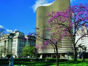 Foto mostra Praça da Liberdade em BH com destaque para o céu aberto e ipês rosas.