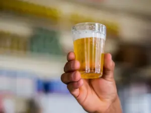 Mão levantando um copo americano de cerveja.