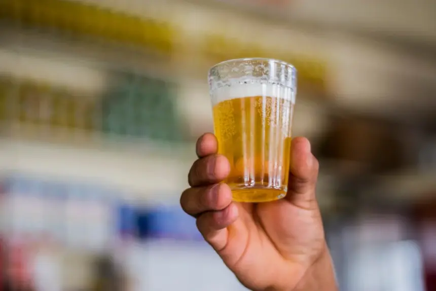 Mão levantando um copo americano de cerveja.