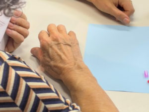 Imagem mostra mão de uma idosa e uma folha.