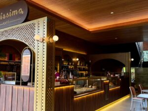 Imagem mostra o interior de uma cafeteria com balcão e mesas.