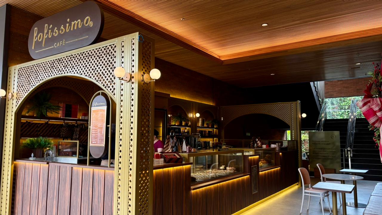 Imagem mostra o interior de uma cafeteria com balcão e mesas.