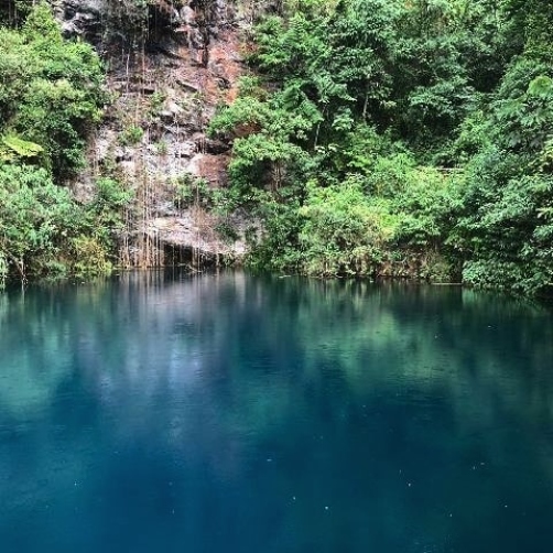 Lago de águas azul-esverdeadas cercado por mata densa e paredão rochoso.