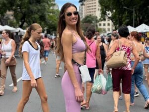 Mulher morena com roupa de academia lilás posando para foto em uma calçada.