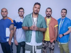 Cinco homens posam lado a lado em estúdio, usando roupas casuais e coloridas,