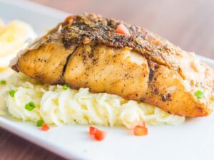 Filé de peixe assado sobre purê de batata, guarnecido com tomate picado e cebolinha.