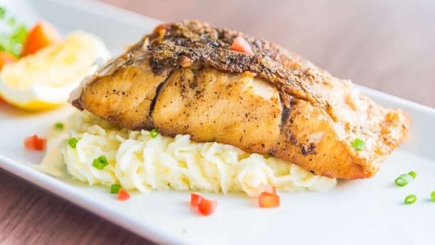 Filé de peixe assado sobre purê de batata, guarnecido com tomate picado e cebolinha.