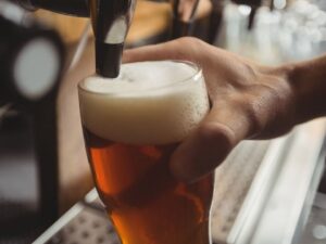 Mão segura um copo de cerveja sendo enchido por uma torneira, com muita espuma.