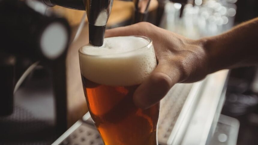 Mão segura um copo de cerveja sendo enchido por uma torneira, com muita espuma.