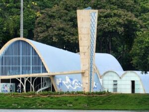Igreja da Pampulha à beira do lago com teto azul e torre clara, cercada por árvores.