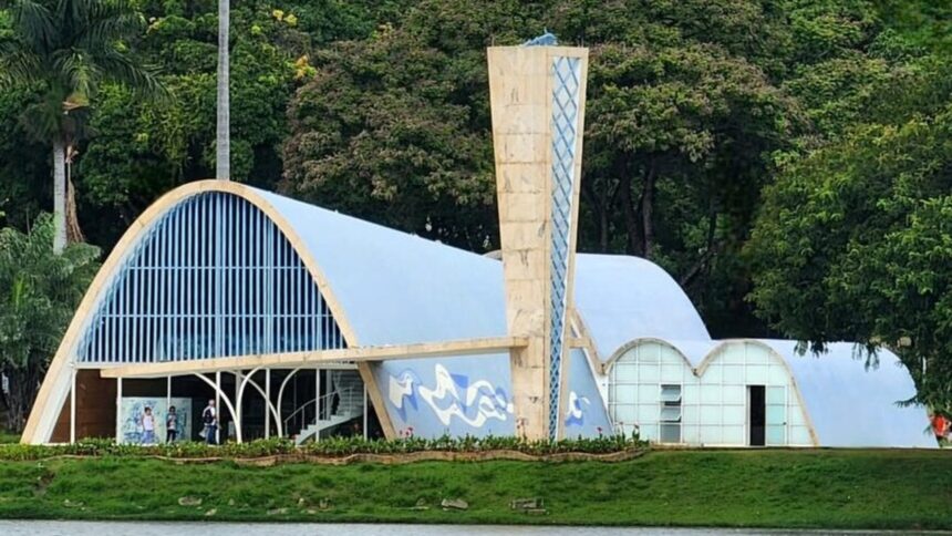 Igreja da Pampulha à beira do lago com teto azul e torre clara, cercada por árvores.