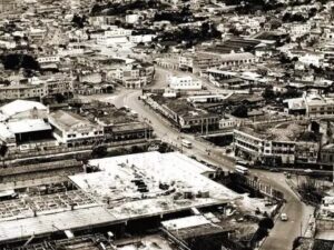 Vista aérea em preto e branco de uma cidade com edifícios, ruas, veículos e canteiro de obras.
