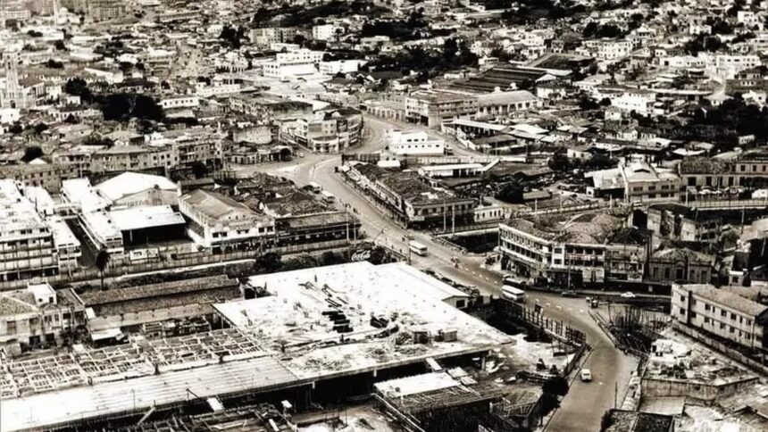 Vista aérea em preto e branco de uma cidade com edifícios, ruas, veículos e canteiro de obras.