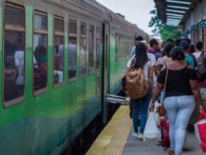 Pessoas embarcando em um trem verde e cinza parado na plataforma da estação.