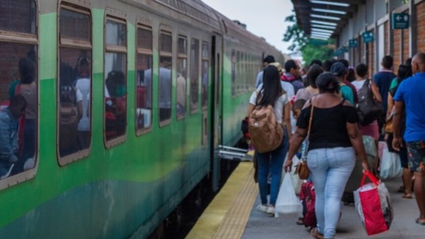 Pessoas embarcando em um trem verde e cinza parado na plataforma da estação.