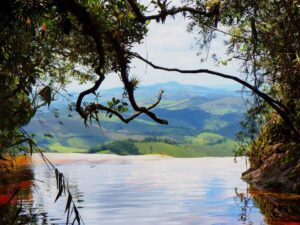 Cena panorâmica de cachoeira com água avermelhada fluindo, emoldurada por folhagem e montanhas distantes.