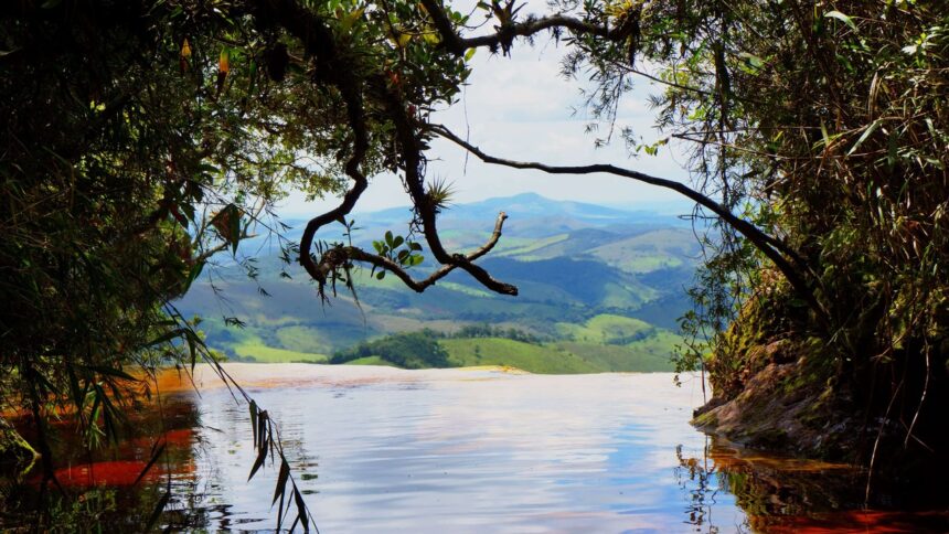 Cena panorâmica de cachoeira com água avermelhada fluindo, emoldurada por folhagem e montanhas distantes.