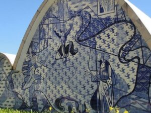 Parede de azulejos azuis e brancos da Igreja da Pampulha com figuras e céu azul.