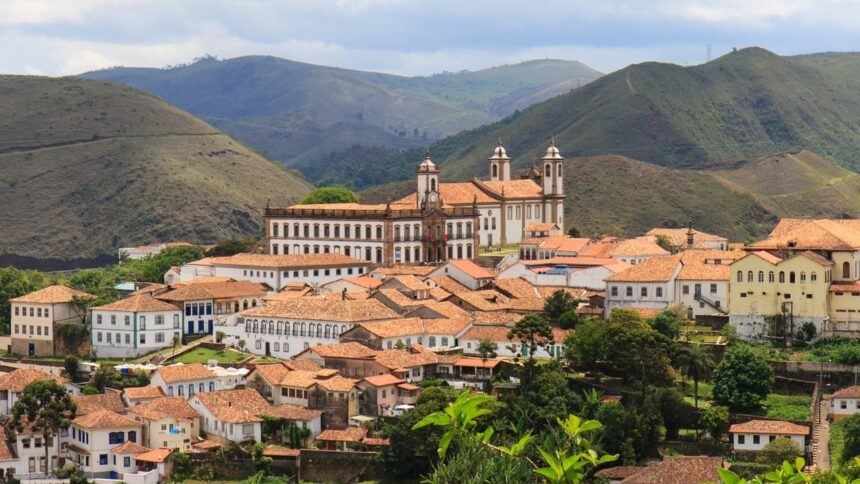 Vista panorâmica de uma cidade colonial com telhados de barro e igrejas brancas, cercada por montanhas.