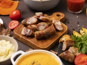 Fatias de linguiça, batatas assadas, purê, abóboras e sopa em uma mesa rústica.