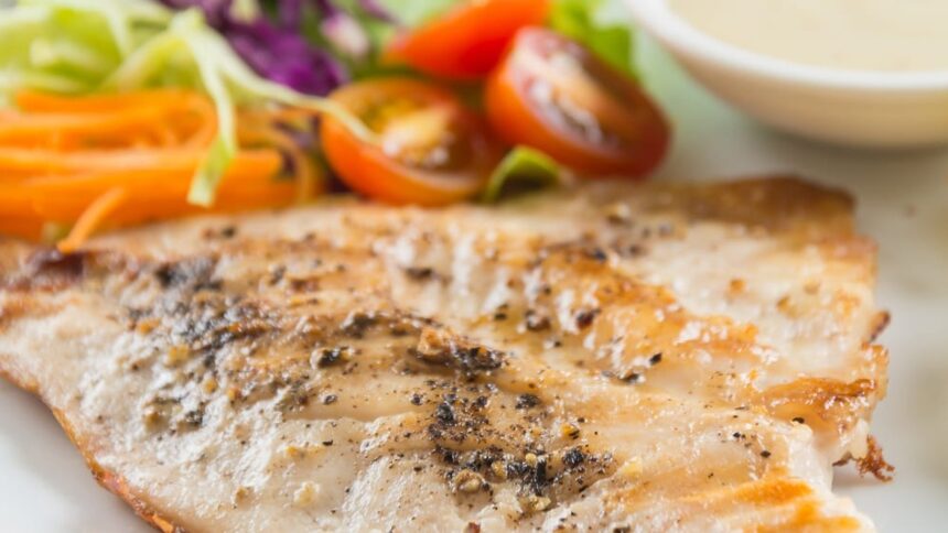 Filé de peixe grelhado com pimenta preta, salada colorida e molho em segundo plano.