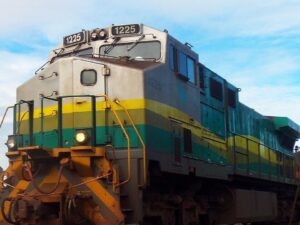 Locomotiva de trem cinza, amarela e verde com o número 1225, sob céu azul claro.