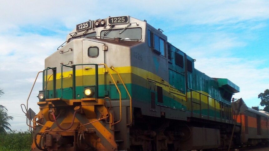 Locomotiva de trem cinza, amarela e verde com o número 1225, sob céu azul claro.