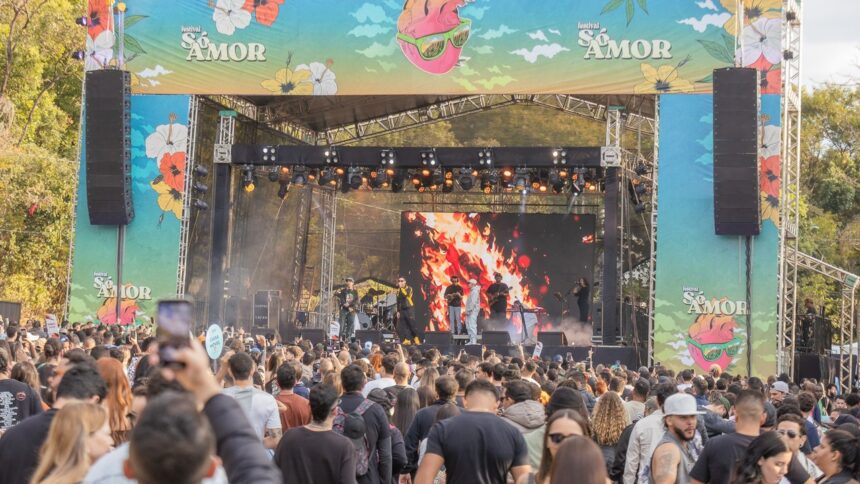 Músicos se apresentam em palco de festival com telão de chamas e público filmando, banners 'Só Amor'.