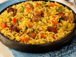 Galinhada caseira com arroz amarelo, frango, pimentões vermelho e verde em panela de barro.