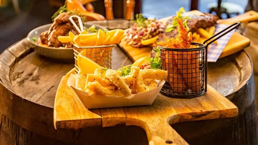 Comida de boteco, incluindo batata frita, lula e camarão frito, em mesa de madeira.