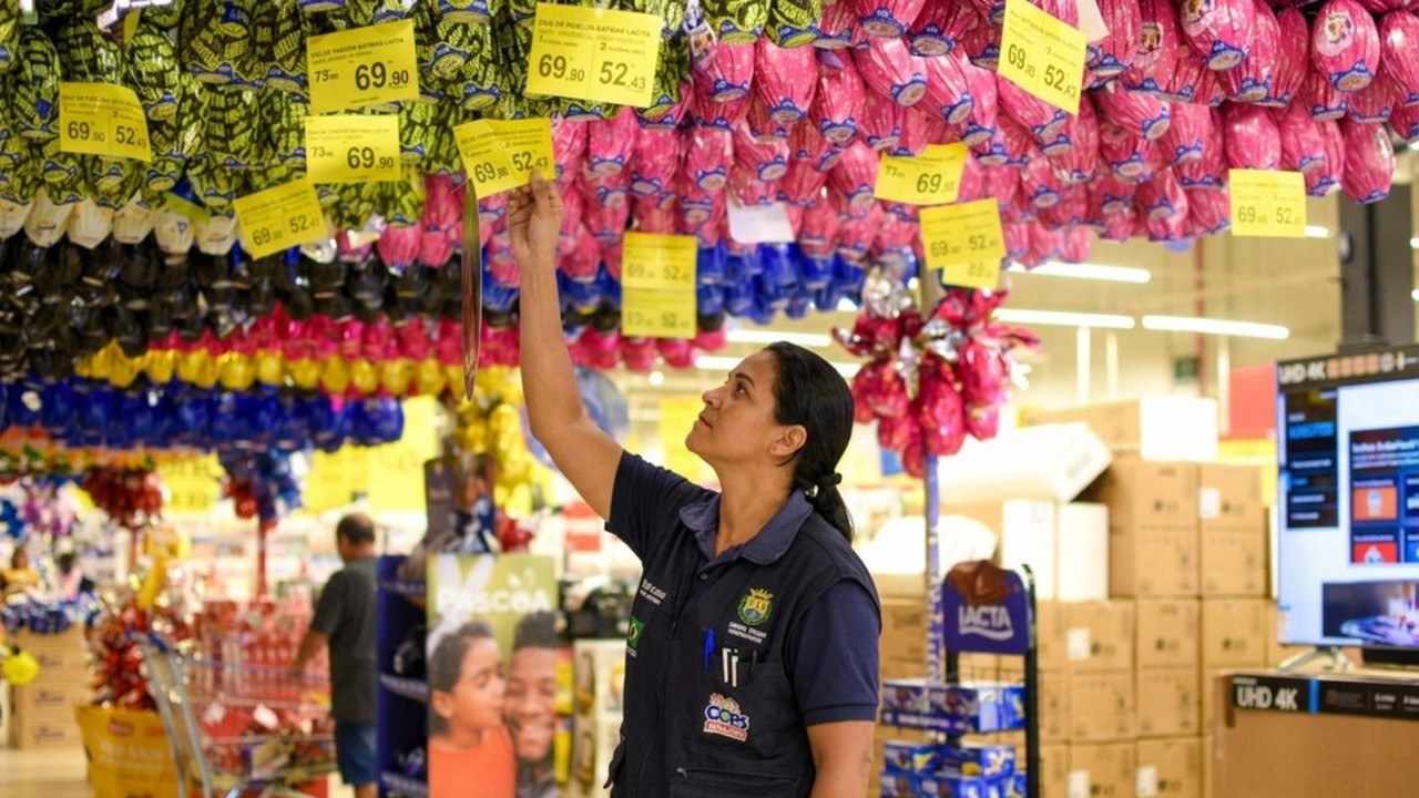 Mulher ajusta etiqueta de preço '69.90' em ovos de Páscoa coloridos em supermercado. - (foto: Divulgação)
