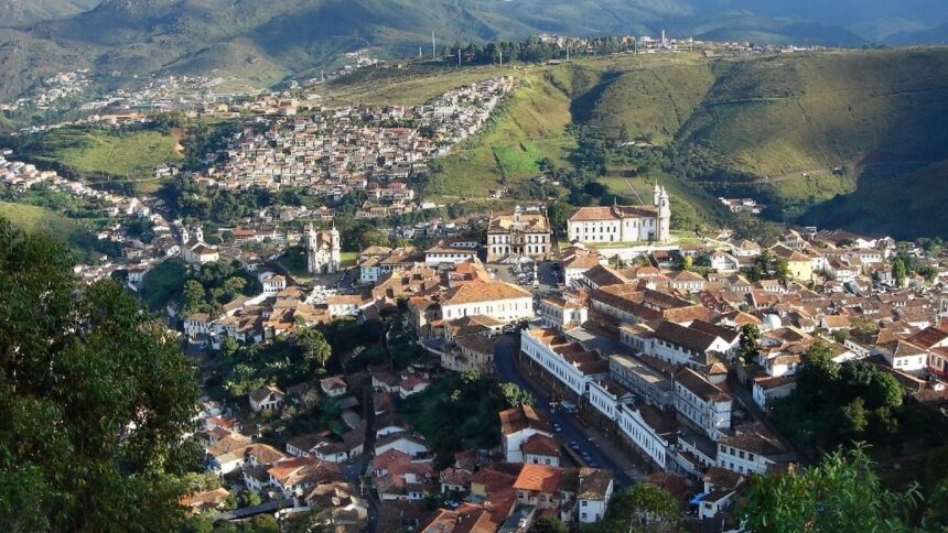 Vista panorâmica de uma cidade colonial com telhados de barro e igrejas brancas em um vale.