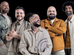 Cinco homens sorrindo, com barbas e cabelo, em fundo preto.
