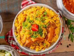 Prato de galinhada mineira em panela de alumínio, com arroz amarelo, frango, cebolinha e pimenta biquinho.