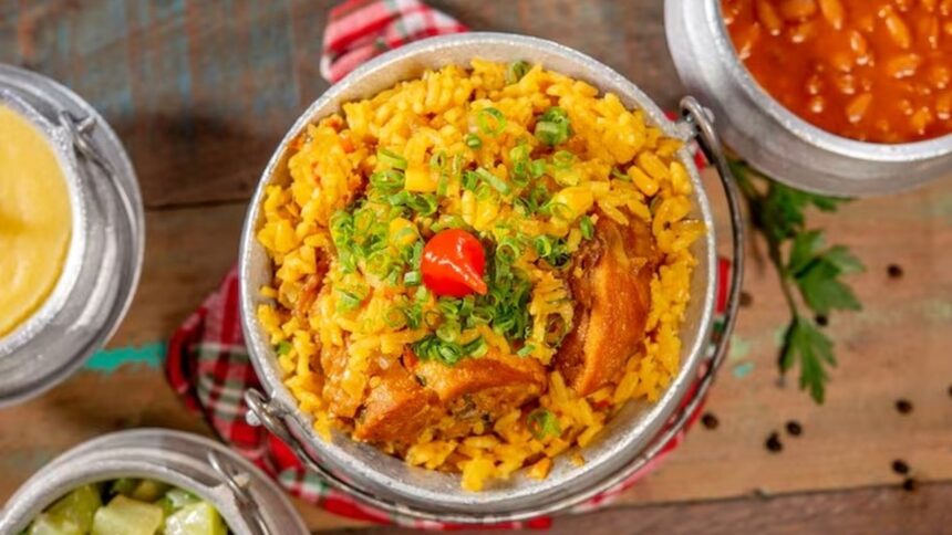 Prato de galinhada mineira em panela de alumínio, com arroz amarelo, frango, cebolinha e pimenta biquinho.