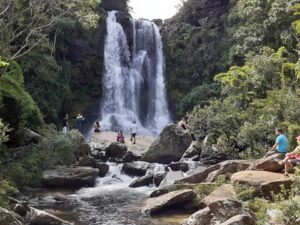 Cachoeira volumosa com várias pessoas em rochas e em seu entorno, cercada por floresta densa.