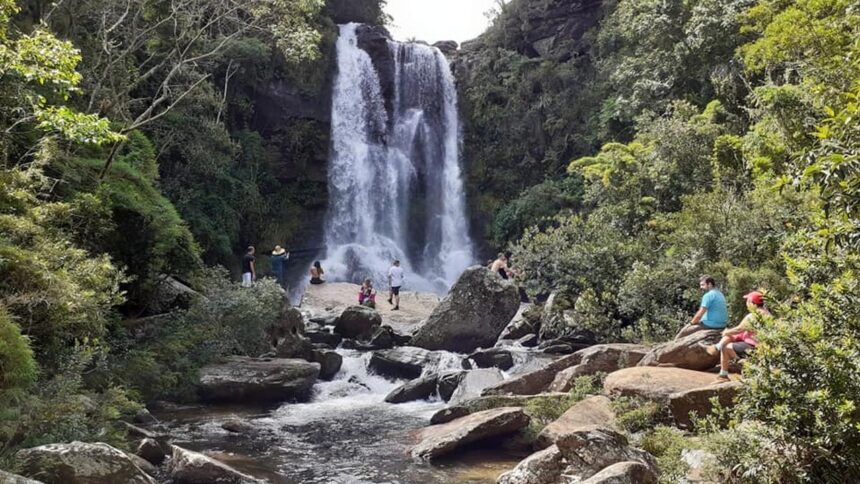 Cachoeira volumosa com várias pessoas em rochas e em seu entorno, cercada por floresta densa.