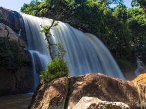 Cachoeira volumosa caindo sobre rochas em meio a vegetação exuberante sob céu azul.