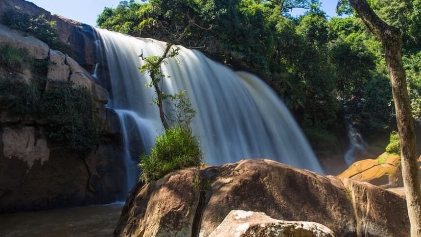 Cachoeira volumosa caindo sobre rochas em meio a vegetação exuberante sob céu azul.