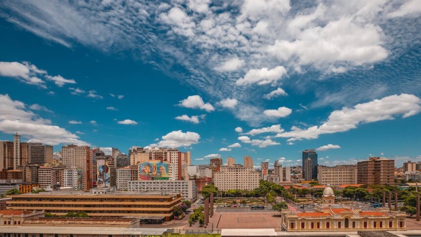 Vista aérea de Belo Horizonte com edifícios, murais coloridos, praça e Estação Central sob céu azul.
