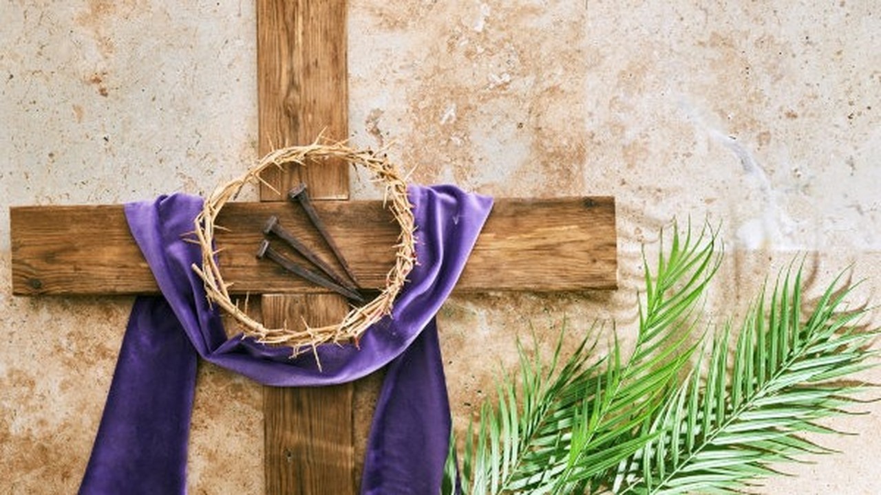 Cruz de madeira com pano roxo, coroa de espinhos, pregos e ramos de palmeira.