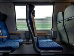 Interior de trem moderno com assentos azuis vazios e paisagem borrada pela janela.